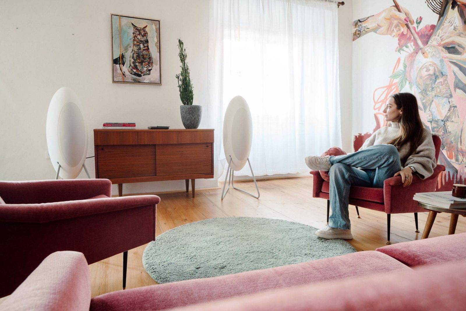 Wohnzimmer mit zwei weißen musegg® High-End-Aktivlautsprechern, eine Frau hört im Sessel Musik
