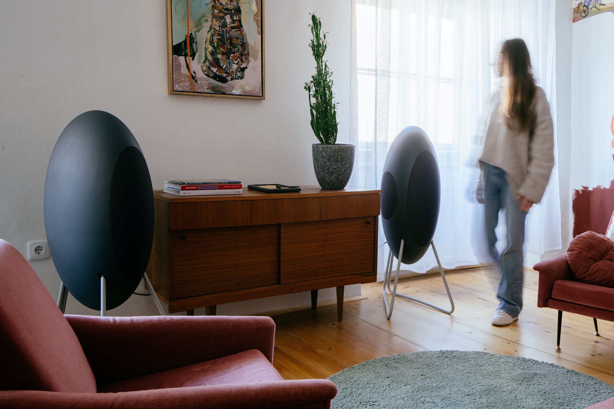 Zwei graphitgraue musegg® neben einem Sideboard im Wohnzimmer, der Tieftöner des rechten Lautsprechers zeigt nach innen